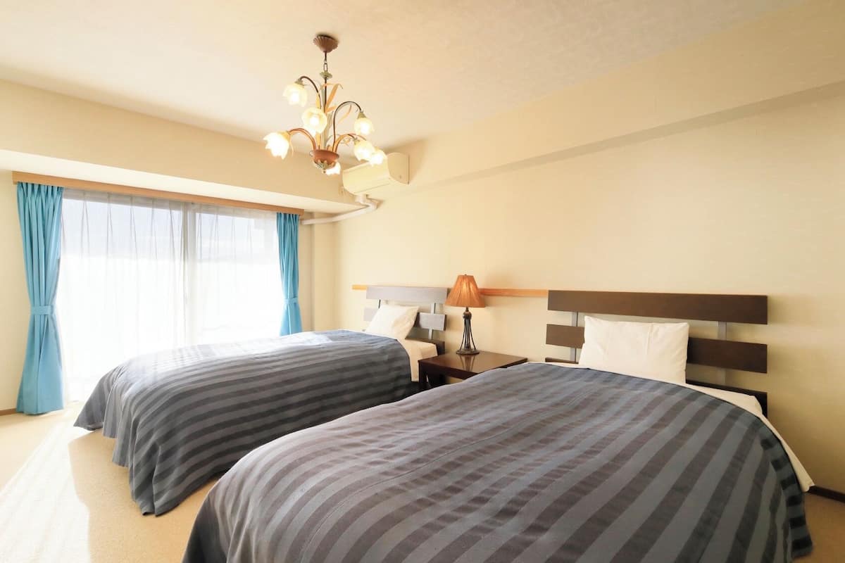 Ein Hotelzimmer mit zwei Betten, einer Deckenleuchte, einem Nachttisch und einem Fenster mit Vorhängen.