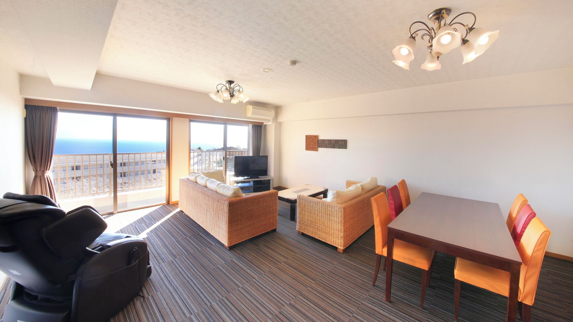 A hotel room with a balcony, a sofa, a dining table, and a television.