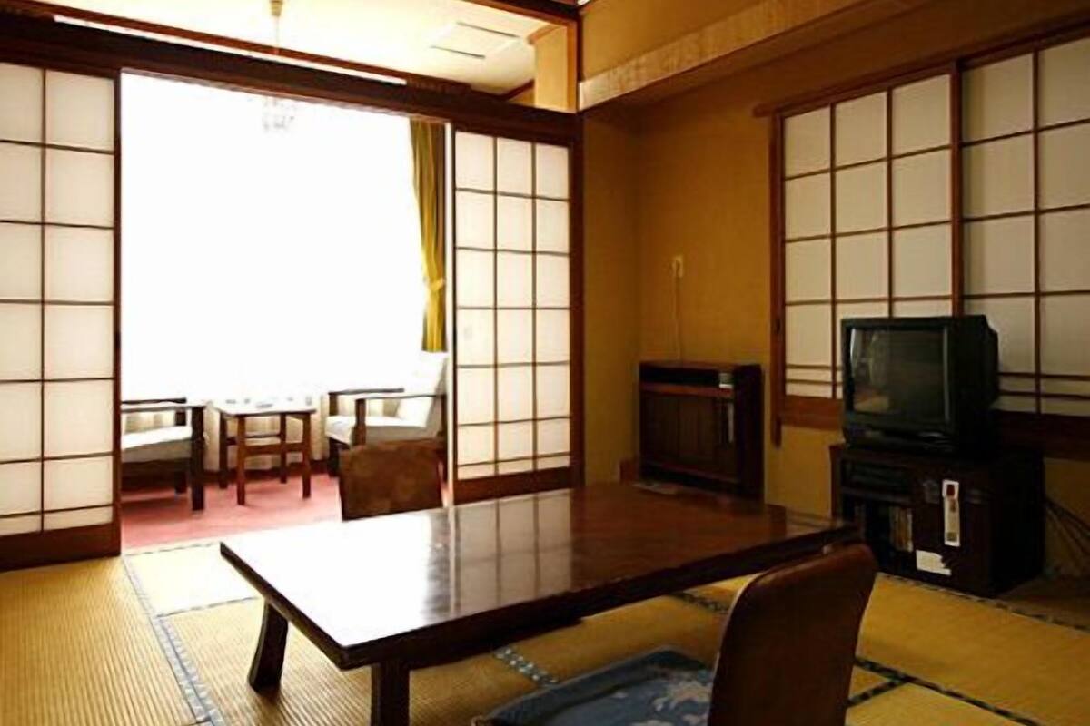A traditional Japanese room with tatami flooring, a low table, a television, and sliding doors.