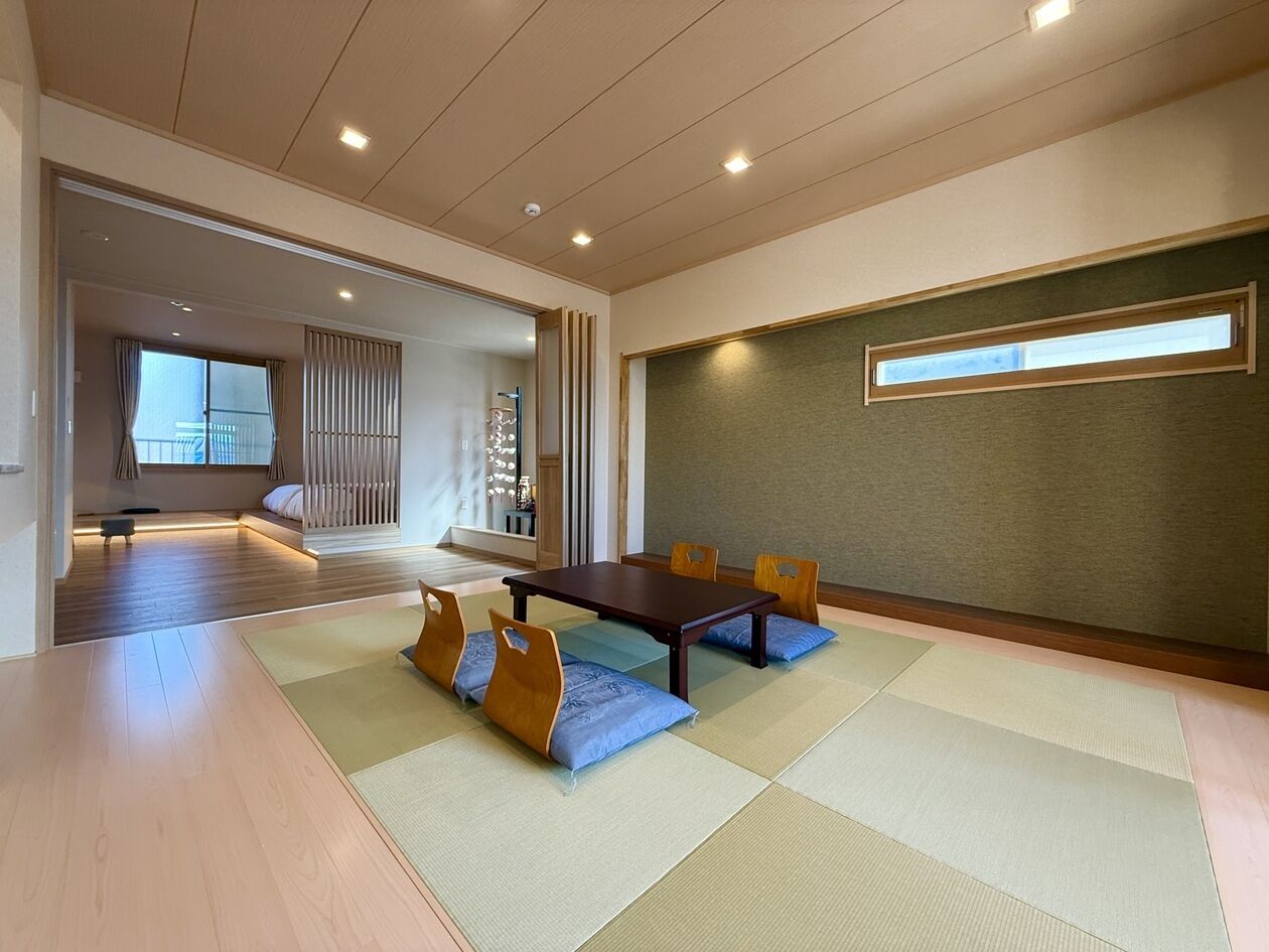 Een traditionele kamer met tatami matten, een lage tafel en stoelen, een schuifdeur naar een andere kamer en uitzicht door een raam.