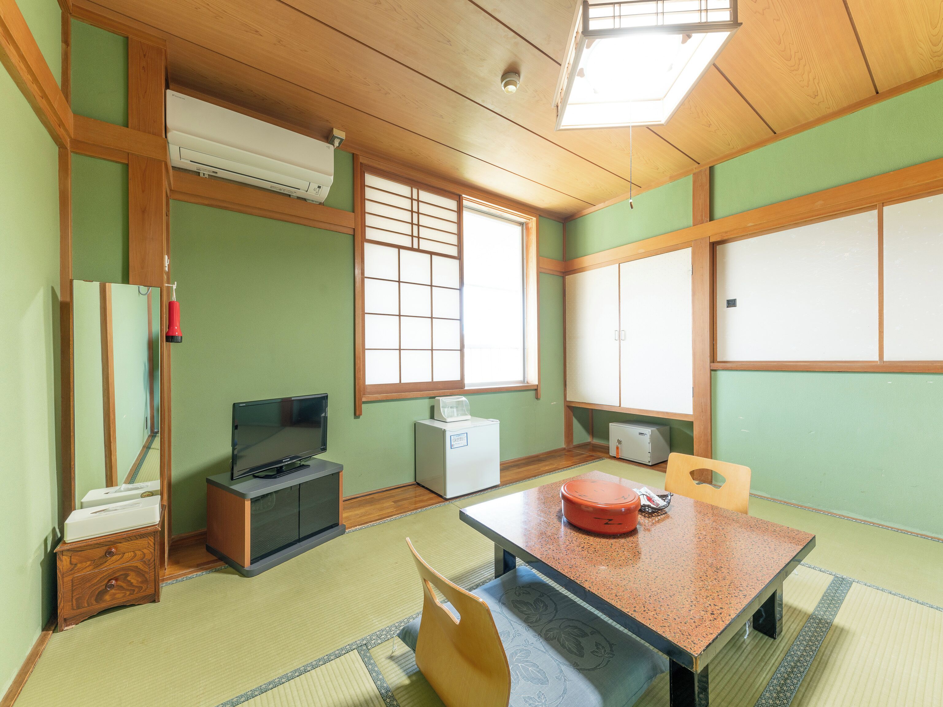 Une pièce de style japonais traditionnel, avec un sol recouvert de tatamis, une table basse, un téléviseur et une fenêtre dotée de panneaux coulissants en papier de riz (shoji).
