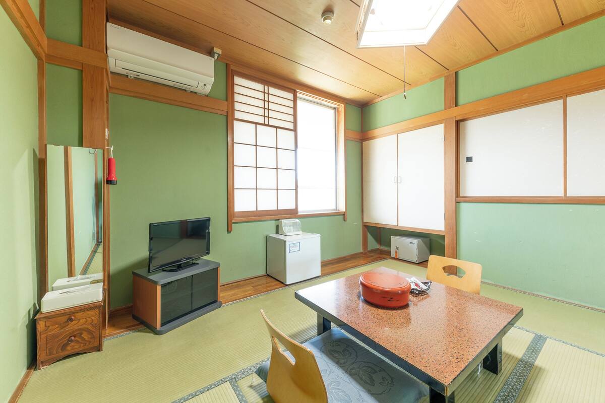 Une pièce de style japonais traditionnel, avec un sol recouvert de tatamis, une table basse, un téléviseur et une fenêtre dotée de panneaux coulissants en papier de riz (shoji).