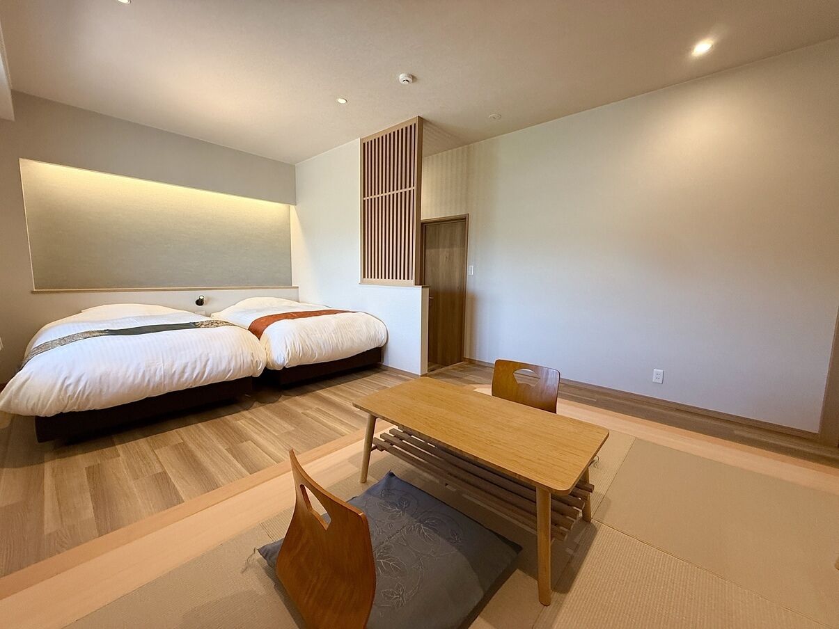 Une chambre d’hôtel moderne équipée d’un lit, d’une table à manger, de chaises, d’un canapé, d’un téléviseur fixé au mur et d’une porte coulissante.