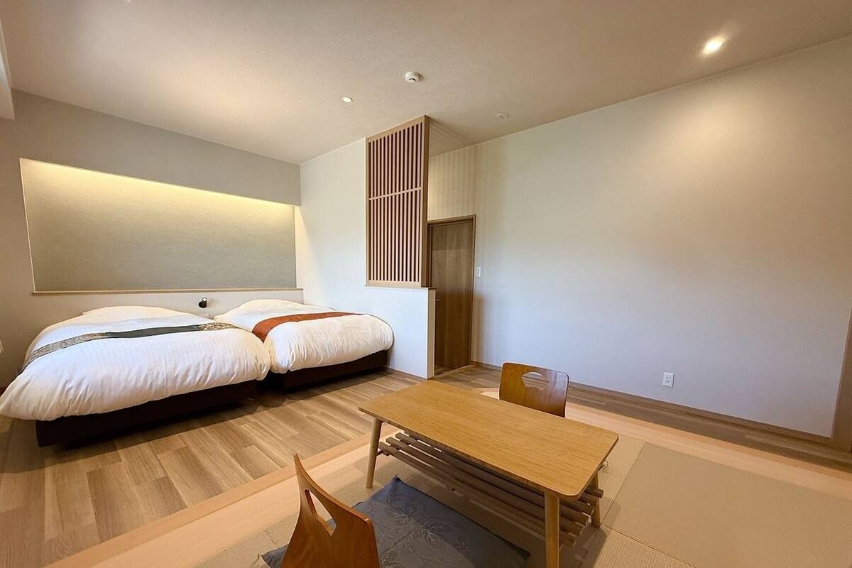 Une chambre d’hôtel moderne équipée d’un lit, d’une table à manger, de chaises, d’un canapé, d’un téléviseur fixé au mur et d’une porte coulissante.