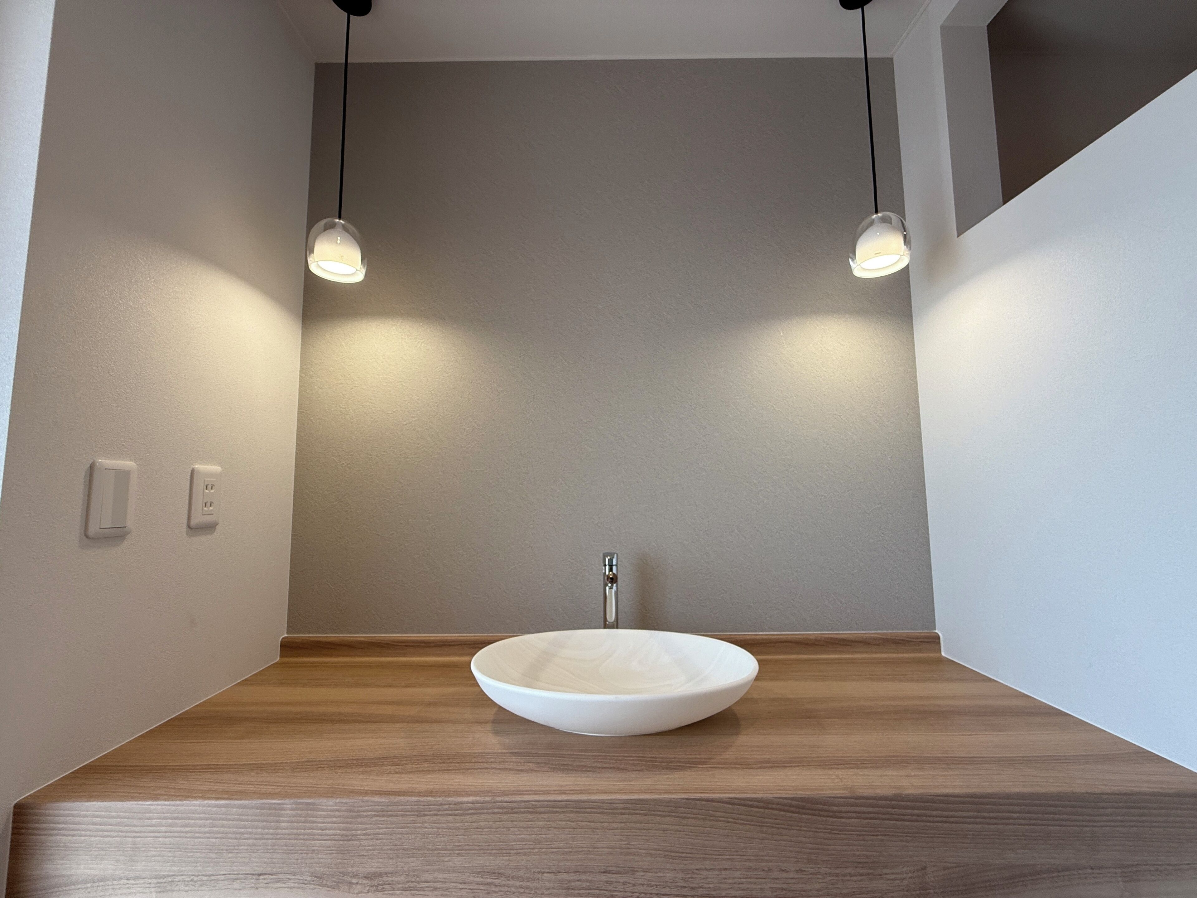 Une salle de bain avec un meuble-lavabo en bois, un lavabo blanc et des luminaires suspendus.