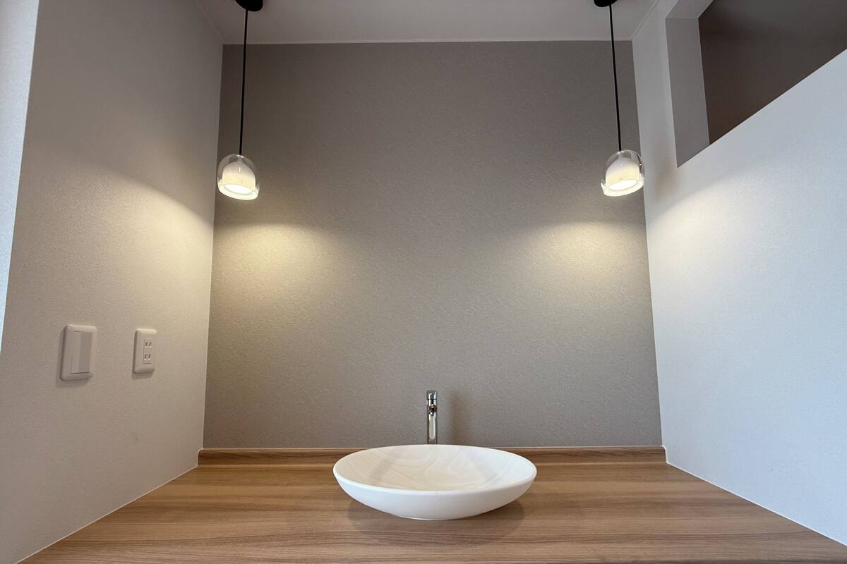 Une salle de bain avec un meuble-lavabo en bois, un lavabo blanc et des luminaires suspendus.