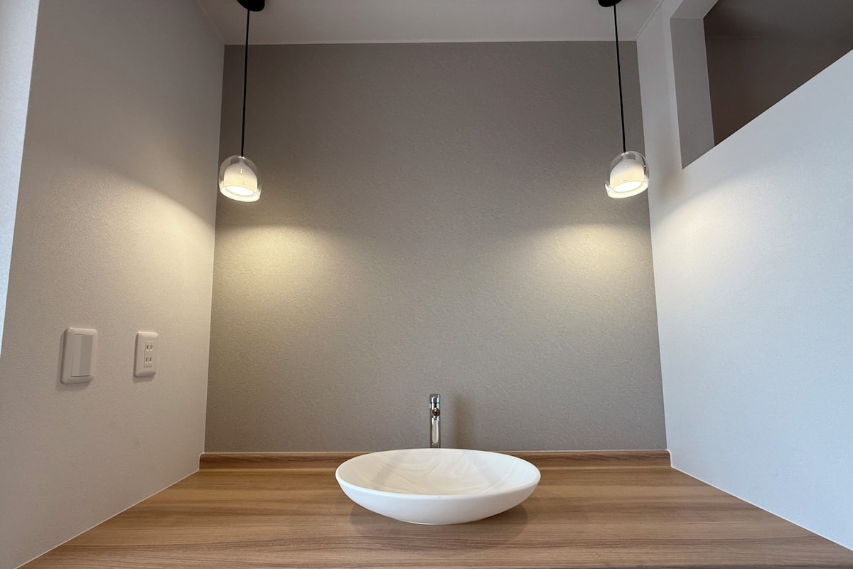Un baño con tocador de madera, lavamanos blanco e iluminación colgante.