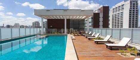A rooftop pool with lounge chairs and a view of the city skyline.