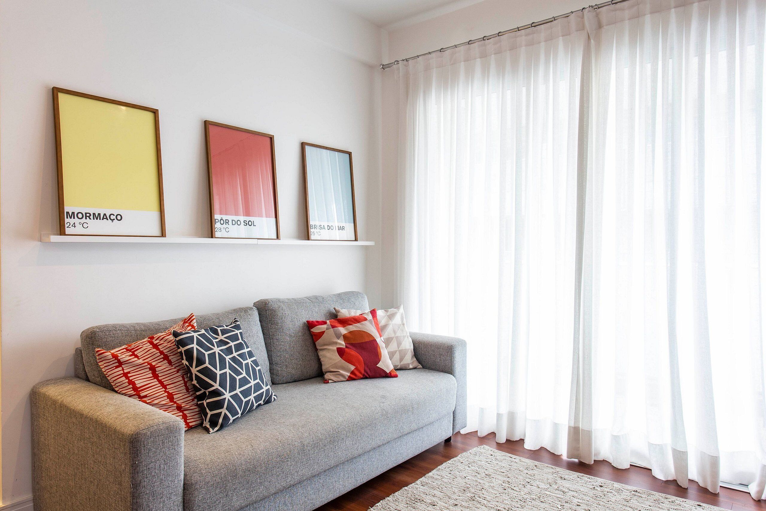 A living room with a grey sofa, colorful cushions, and three framed artworks on the wall.