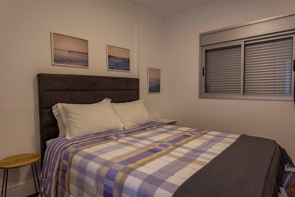 Une chambre à coucher avec un lit, une table de chevet et une fenêtre avec des stores.