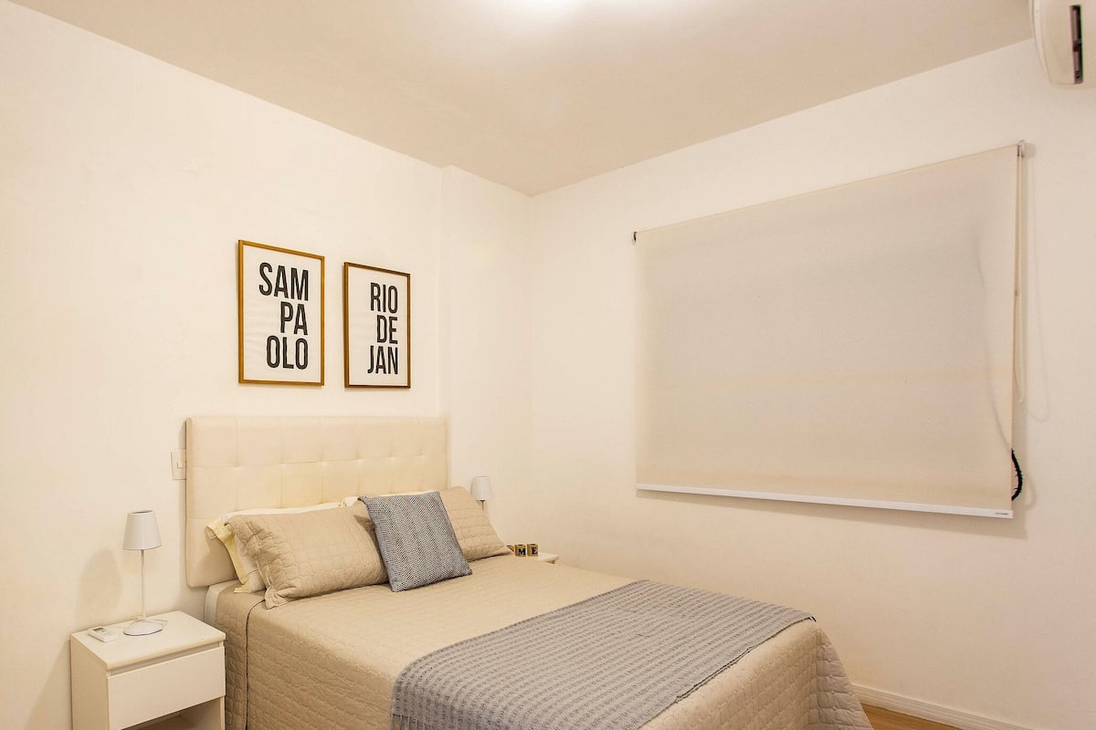 Une chambre à coucher avec un lit, une table de chevet, une lampe et deux panneaux encadrés accrochés au mur.