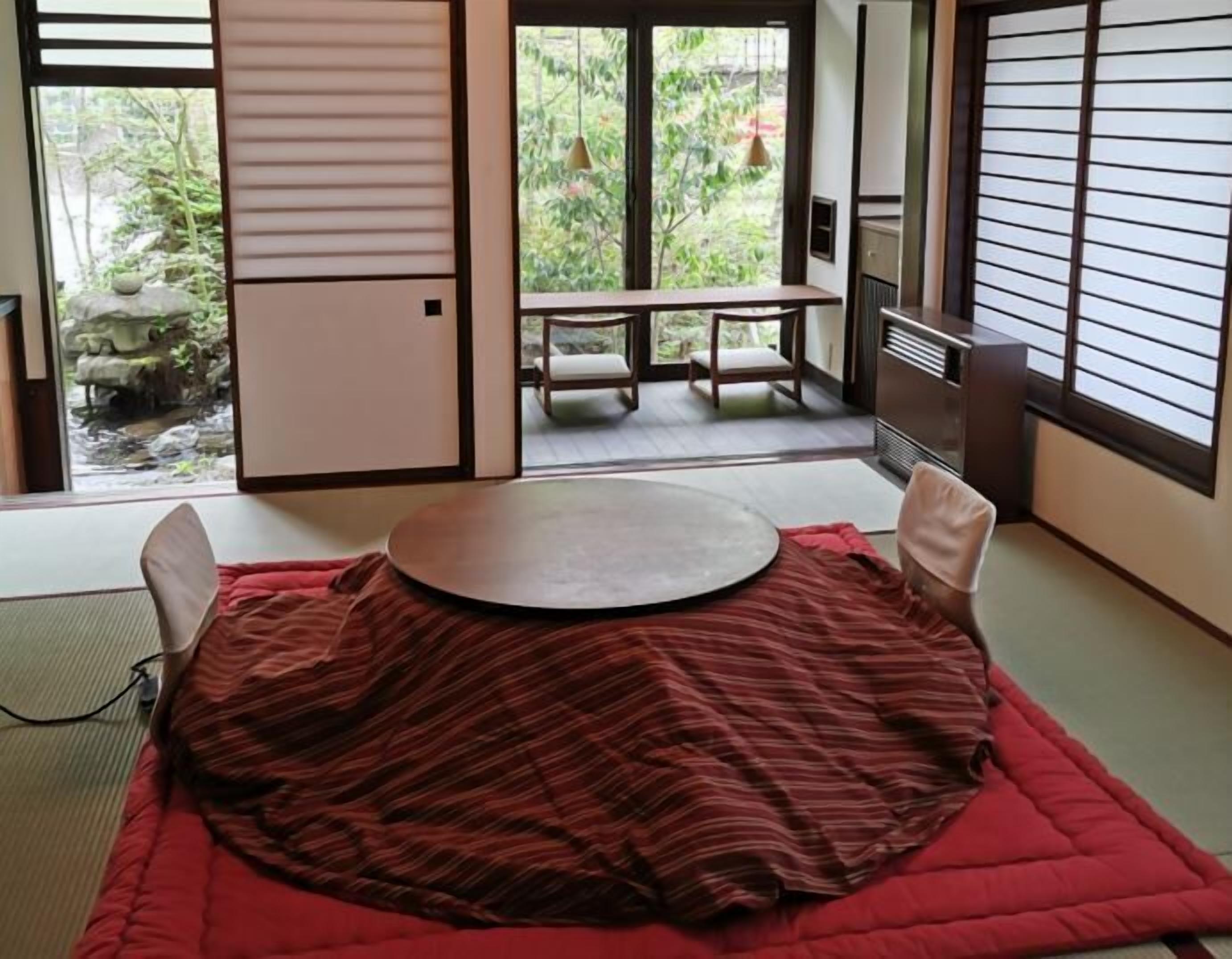 A tatami mat room with a low table, sliding doors, and a view of greenery outside.