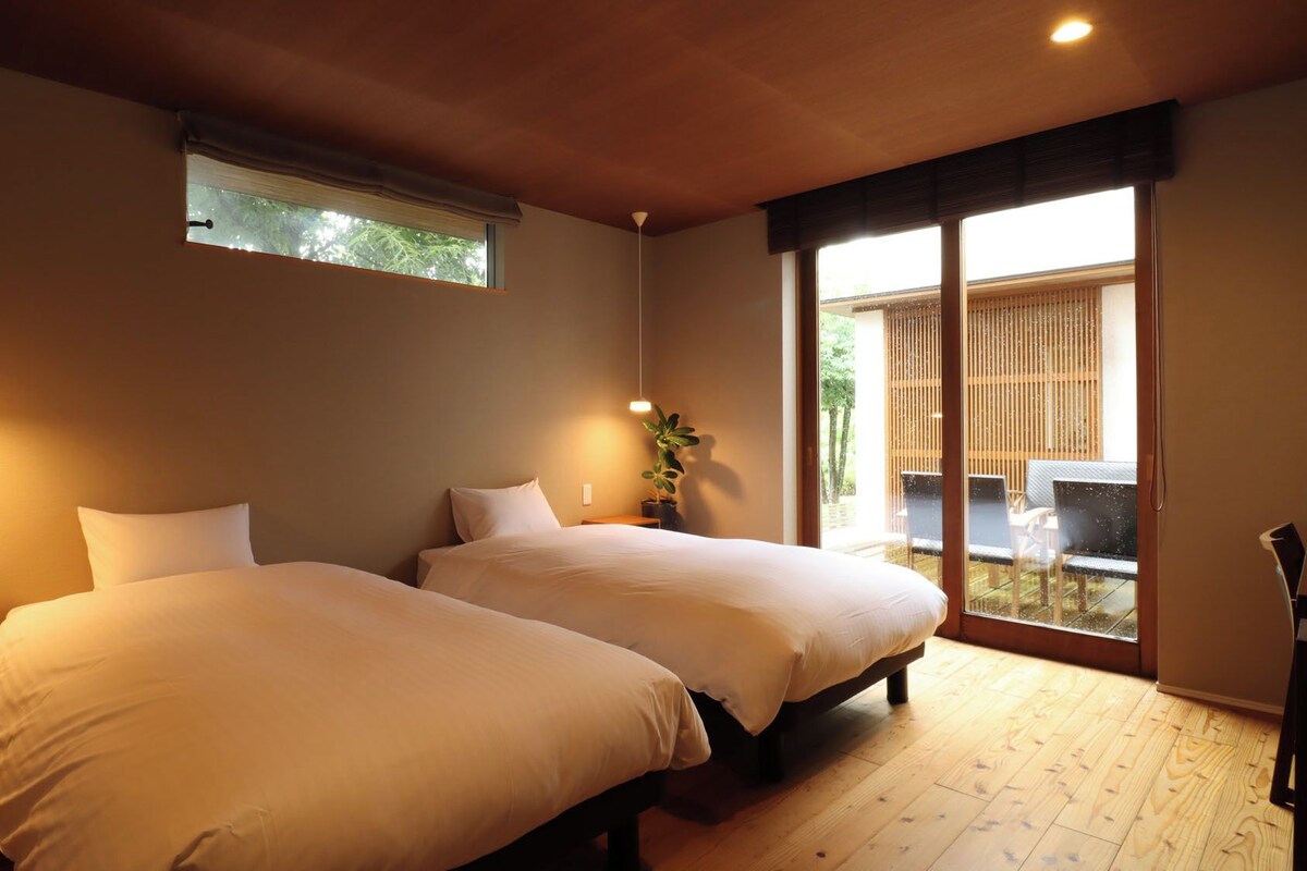 A room with two beds, a window, and a view of the outside.