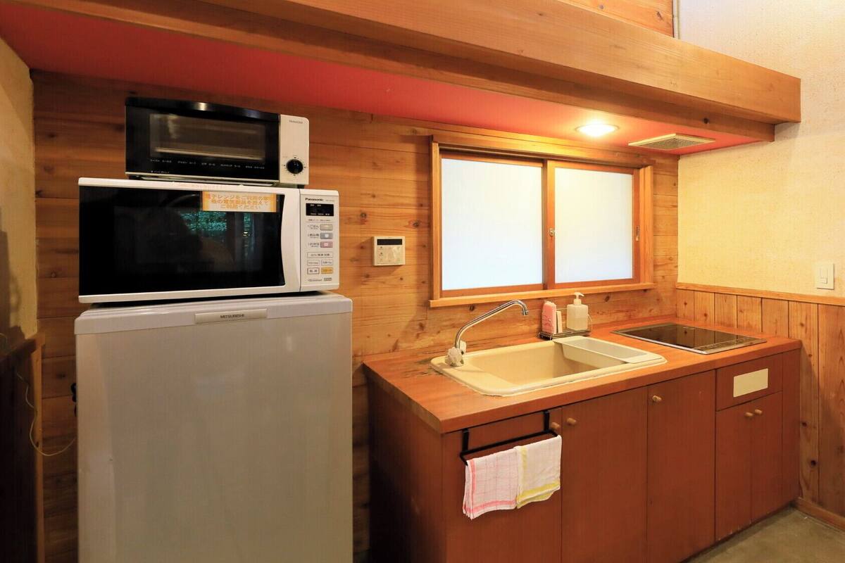Cocina compacta con microondas, refrigerador, pileta y alacenas de madera.