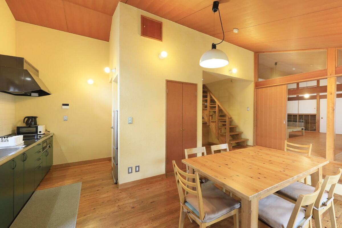 Una cocina amplia con armarios de madera, un comedor con mesa y sillas de madera, y una escalera que conduce a otro nivel.