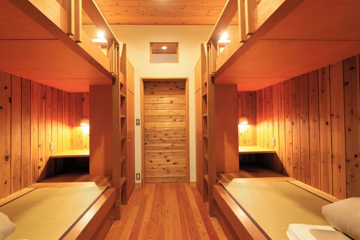 Filas de cabañas de madera con camas individuales y luces fijadas a la pared.