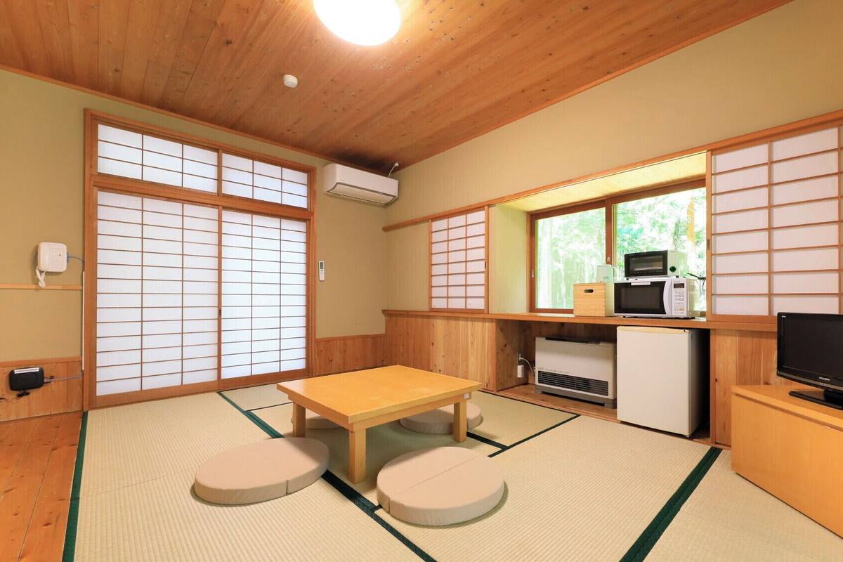 Una habitación japonesa tradicional con suelo de tatami, una mesa baja con cojines, un televisor, un microondas y un refrigerador.