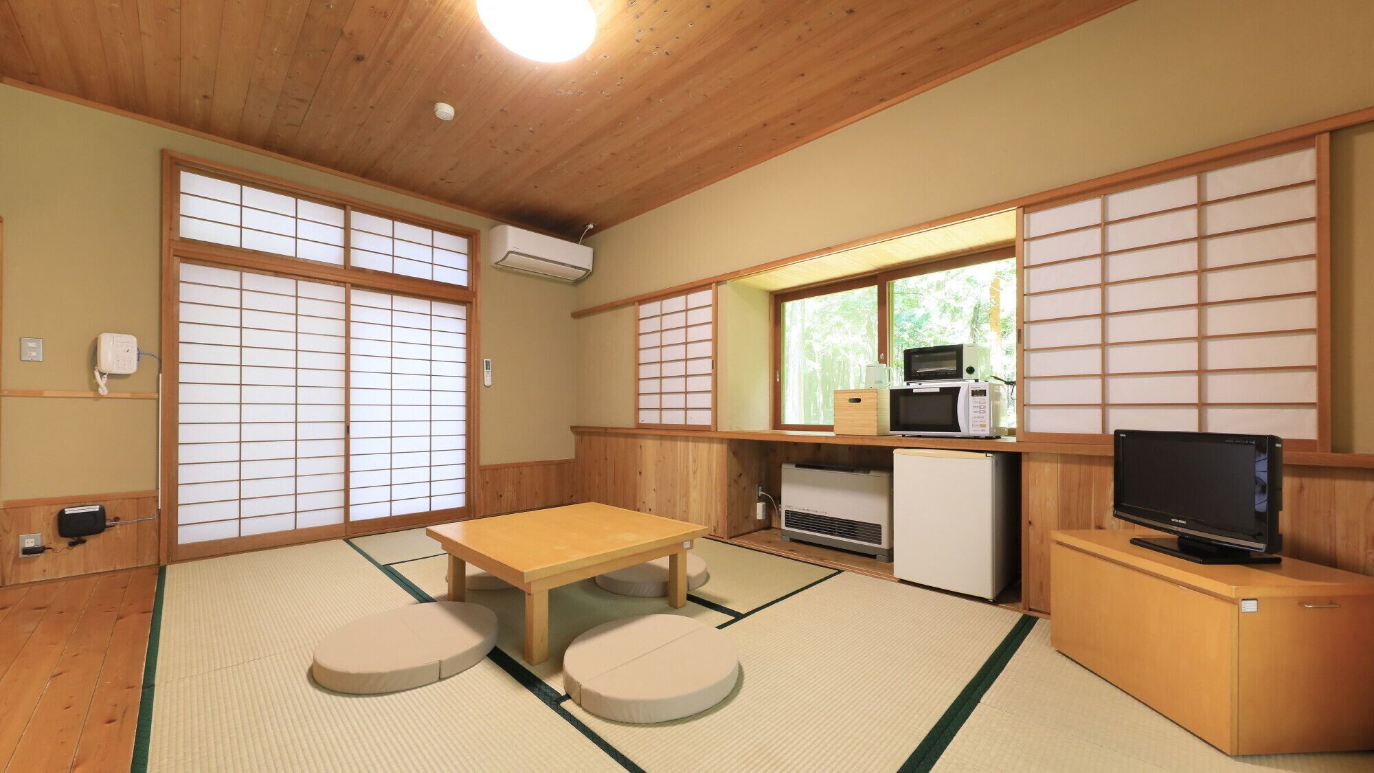 Una habitación de estilo japonés tradicional con suelo de tatami, una mesa baja con cojines, un refrigerador, un microondas y un televisor.
