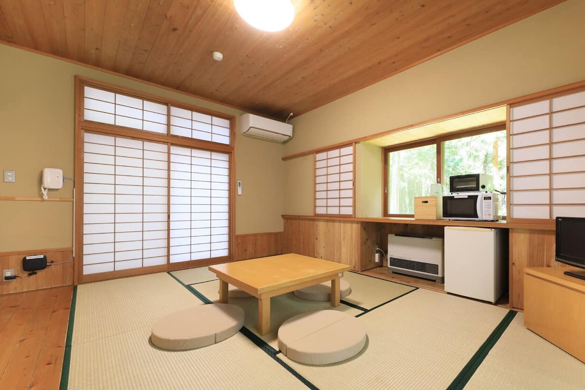 Una habitación de estilo japonés tradicional con suelo de tatami, una mesa baja con cojines, un refrigerador, un microondas y un televisor.