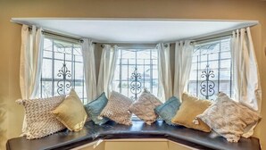 Une baie vitrée agrémentée d’une banquette, de rideaux et de coussins décoratifs.
