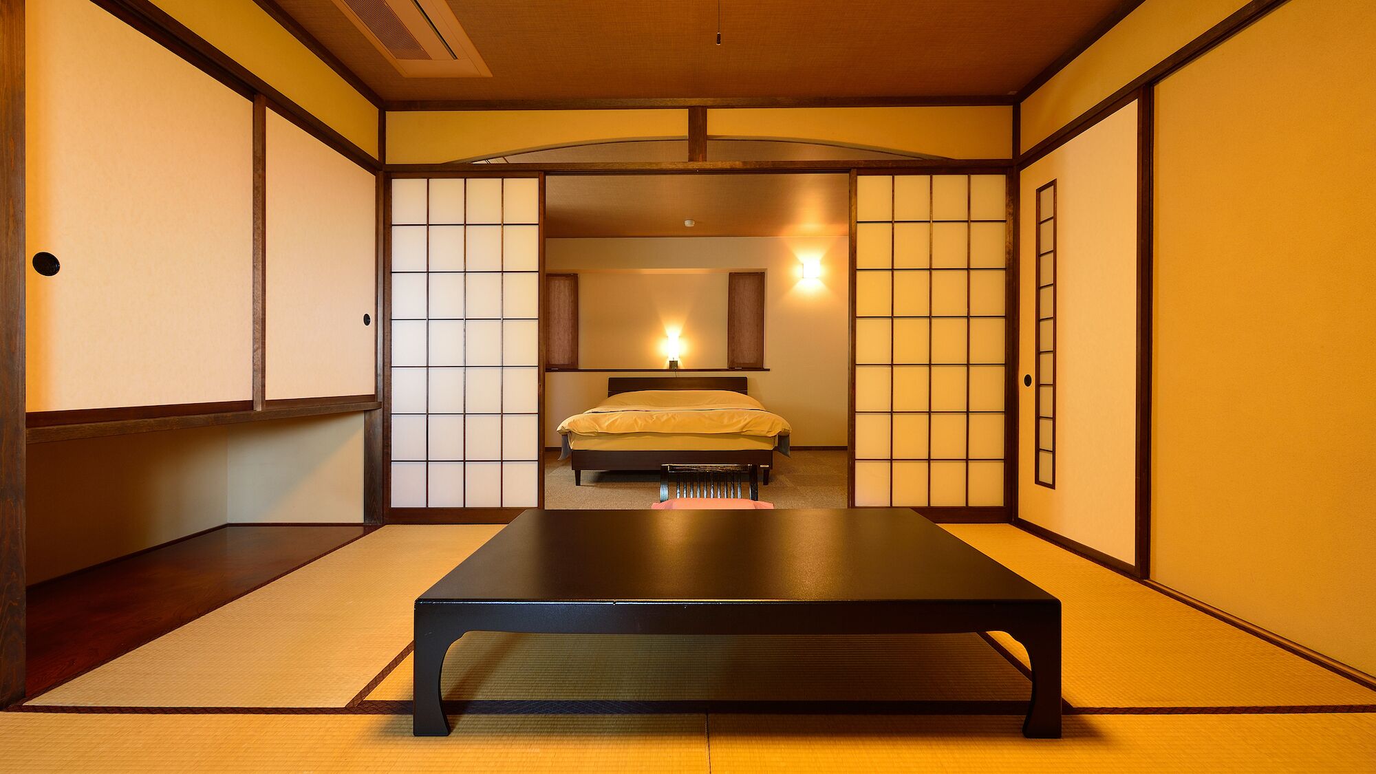A traditional Japanese-style room with tatami flooring, a bed with a yellow bedspread, sliding shoji doors, and a wooden ceiling.