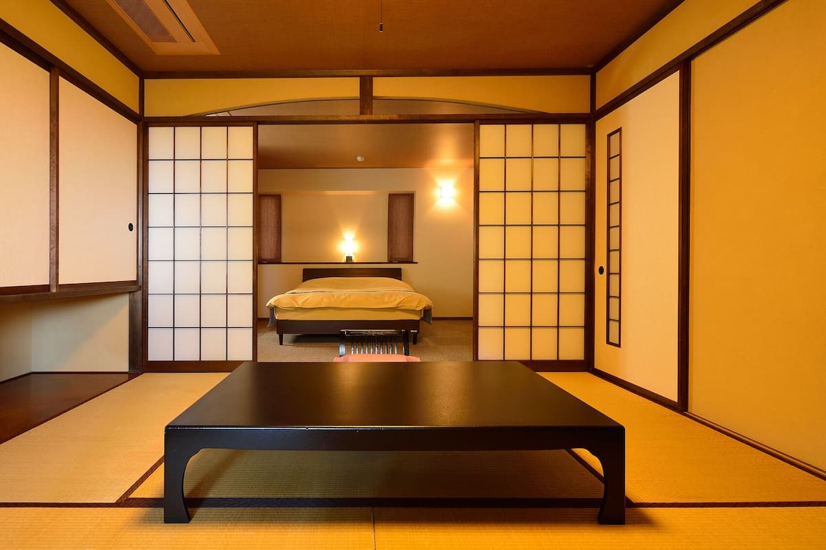 A traditional Japanese-style room with tatami flooring, a bed with a yellow bedspread, sliding shoji doors, and a wooden ceiling.