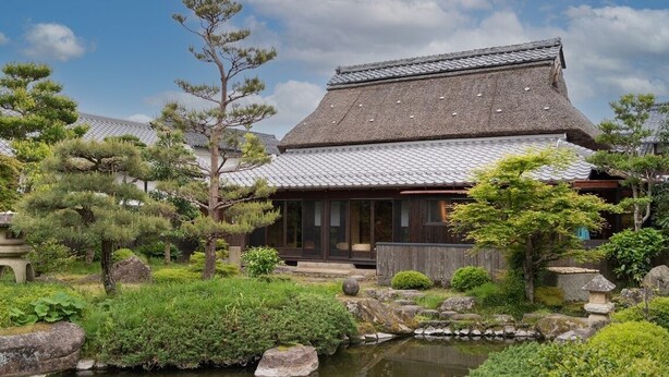 A traditional Japanese building with a tiled roof, surrounded by a garden with rocks, trees, and a small pond. - Nipponia Gokasho Omi Merchant's Town (Higashiomi)