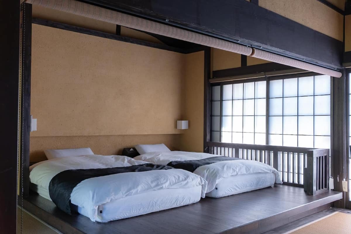 A room with two beds, a large window with a view, and a wooden ceiling structure.