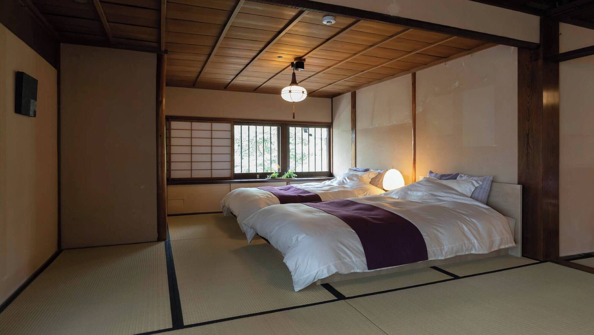 Un dormitorio de estilo japonés tradicional con suelo de tatami, techo bajo y ventana con celosía shoji.