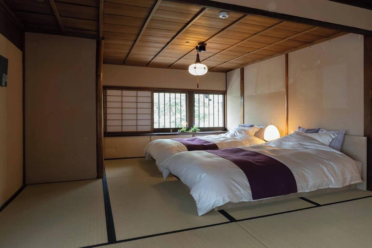 A traditional Japanese-style bedroom with tatami flooring, a low ceiling, and a shoji screen window.