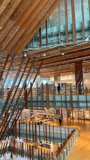 Une bibliothèque à plusieurs niveaux, avec des poutres en bois, des étagères et un escalier central.