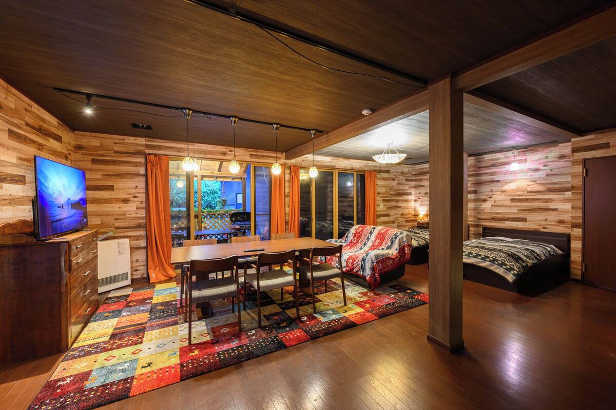 A cozy room with a wooden floor, a dining table, chairs, a bed, and a TV.