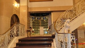 Una imponente escalera con barandillas de metal ornamentadas, una estatua y un fondo decorativo con luces.