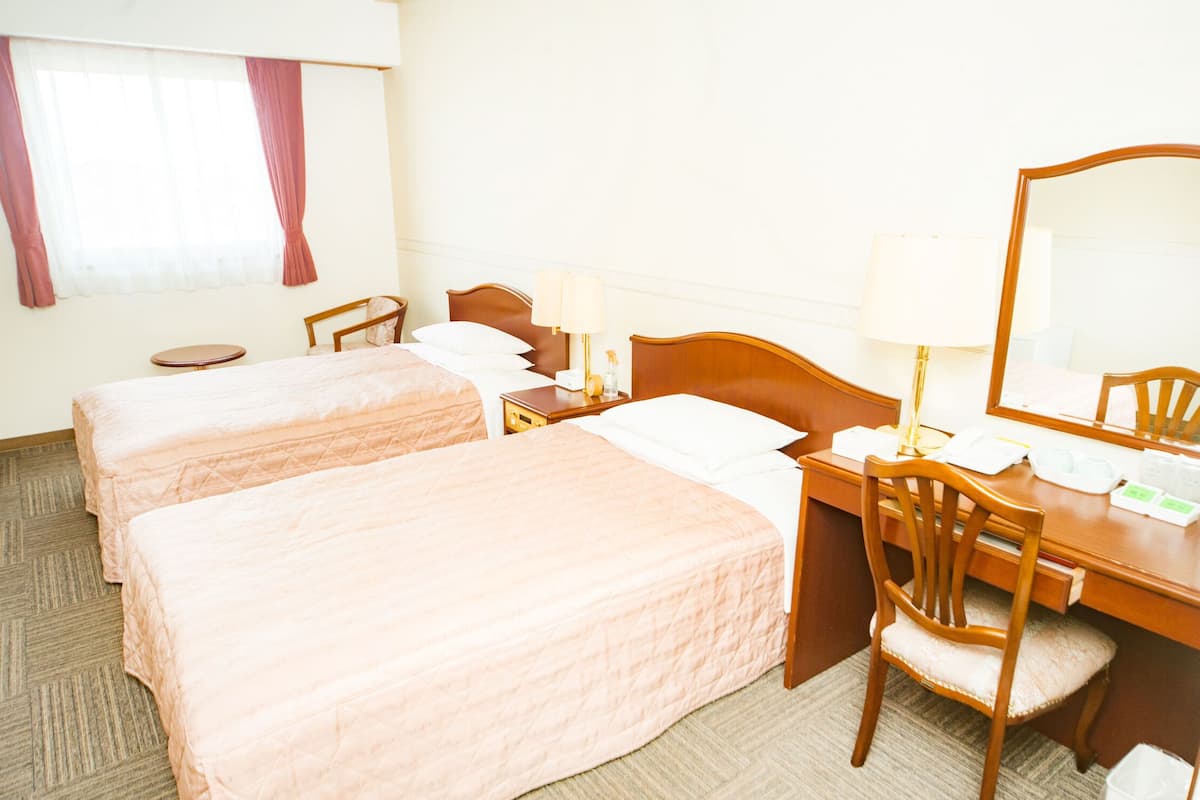 A hotel room with two beds, a desk with a chair, a round table, and a large mirror.