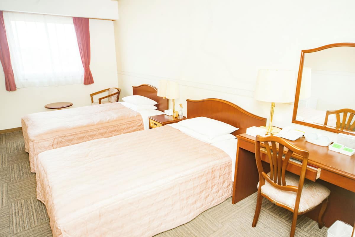A hotel room with two beds, a desk with a chair, a round table, and a large mirror.