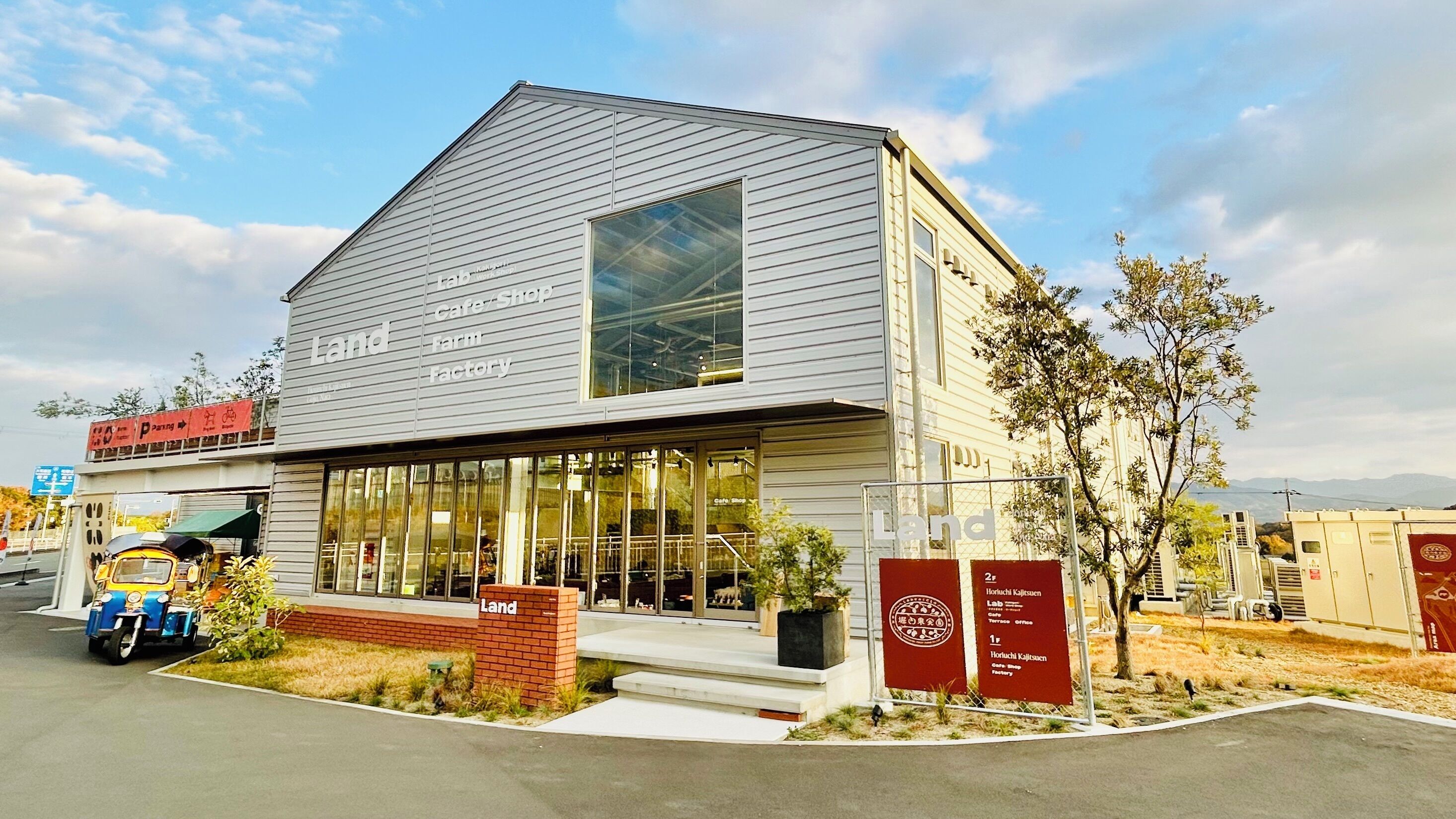 A building with a large glass window, a sign reading 'Land,' and a small brick structure in front.