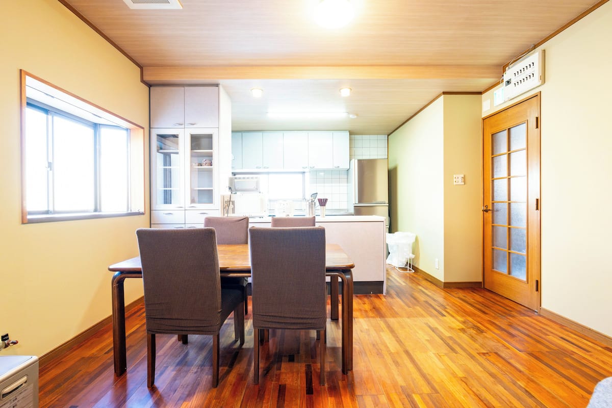 A dining area with a wooden table and chairs, a kitchen in the background, and a door with a frosted glass panel.