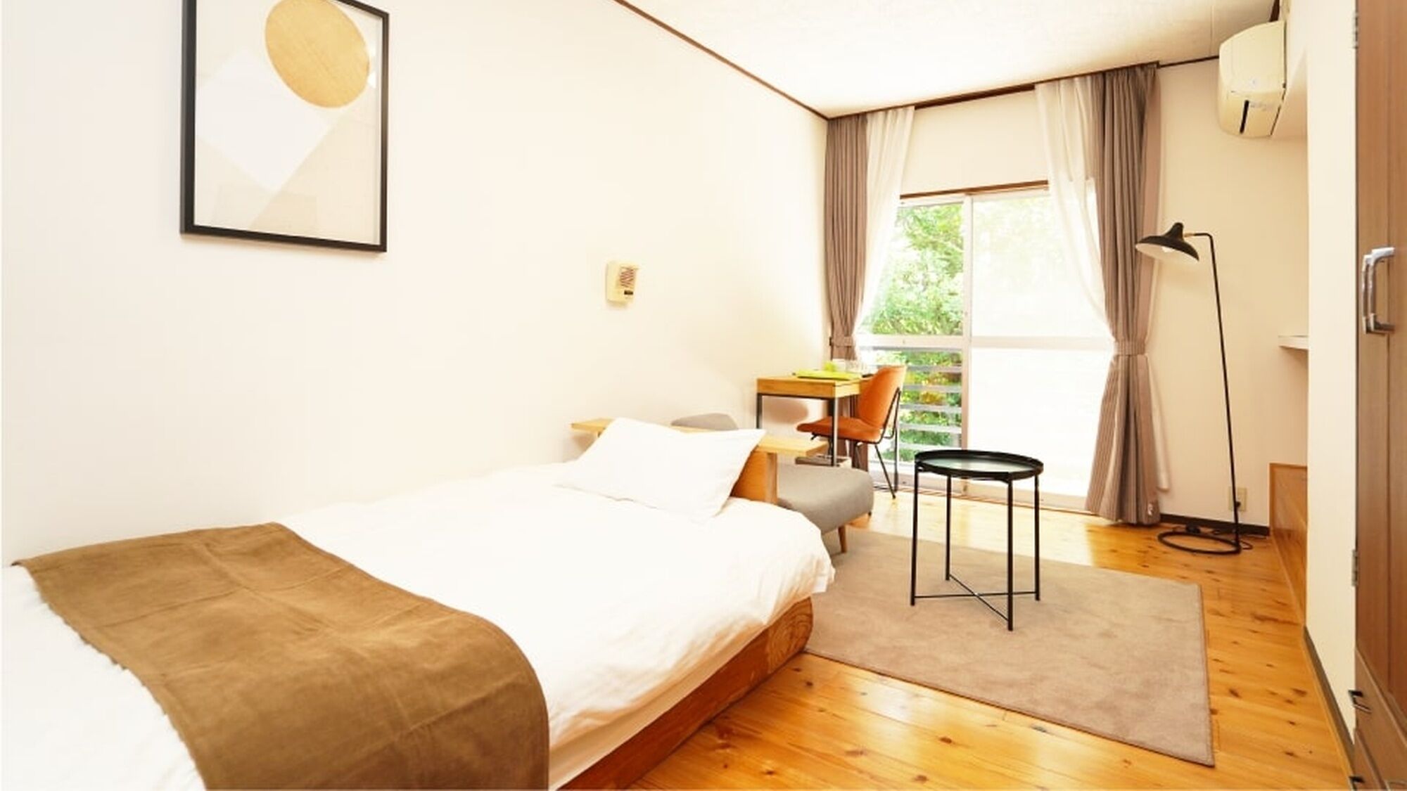 Une chambre à coucher comprenant un lit, un bureau, une chaise, un lampadaire et une fenêtre avec des rideaux.