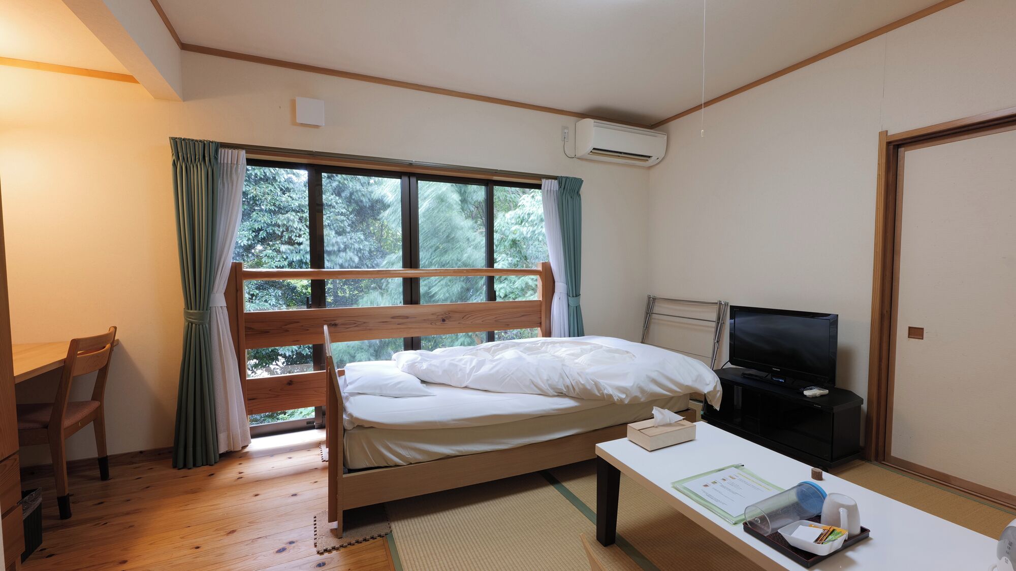 Una habitación con cama, escritorio, televisor y ventana con cortinas.