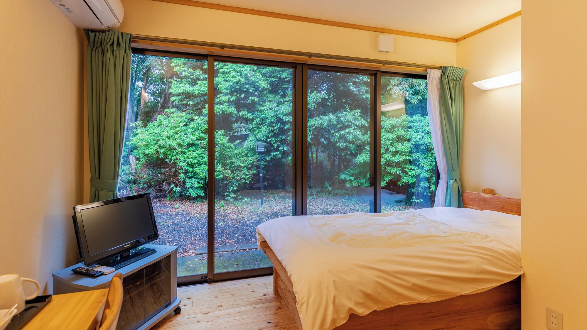 Un dormitorio con cama, televisor sobre un mueble bajo y un ventanal con cortinas.