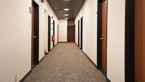 A long, narrow hallway with carpeted floors, doors on both sides, and ceiling lights. - Ai Wellness Izu Kogen Fasting Hotel (Ito)