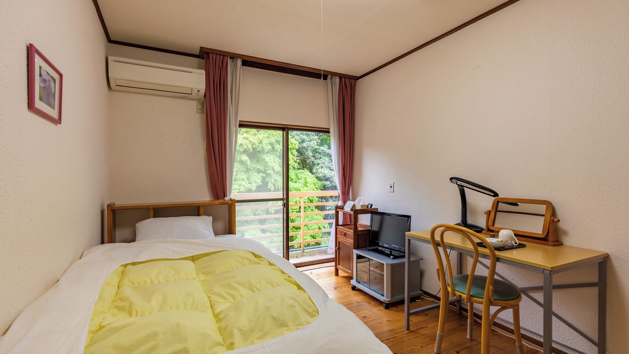 Un dormitorio con cama, escritorio, silla, computadora y ventana con cortinas.