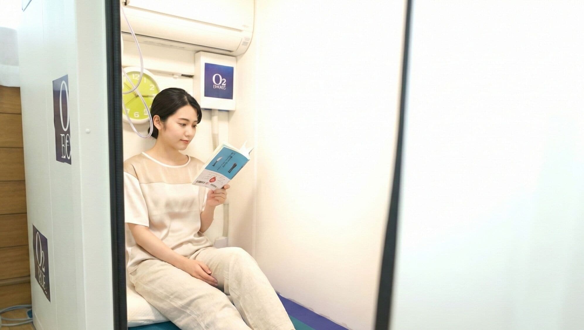 A person seated in a room with a clock, a sign with 'O2' and 'BNAEG' on the wall, and a book in hand.