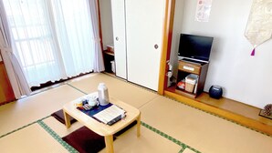 A traditional Japanese room with tatami flooring, a low wooden table with tea set, a television, and a sliding door.