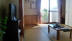 A room with tatami flooring, a television on a cabinet, a sliding door to a balcony, and a table with tea set.