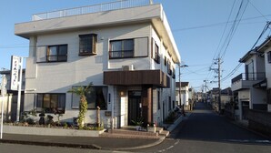 A two-story residential building with a balcony, a gated entrance, and a small garden area.