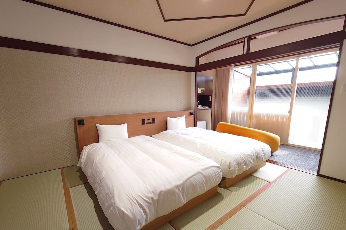 Une chambre d’hôtel avec un grand lit, une petite table, une chaise et une porte-fenêtre coulissante donnant sur un espace extérieur.
