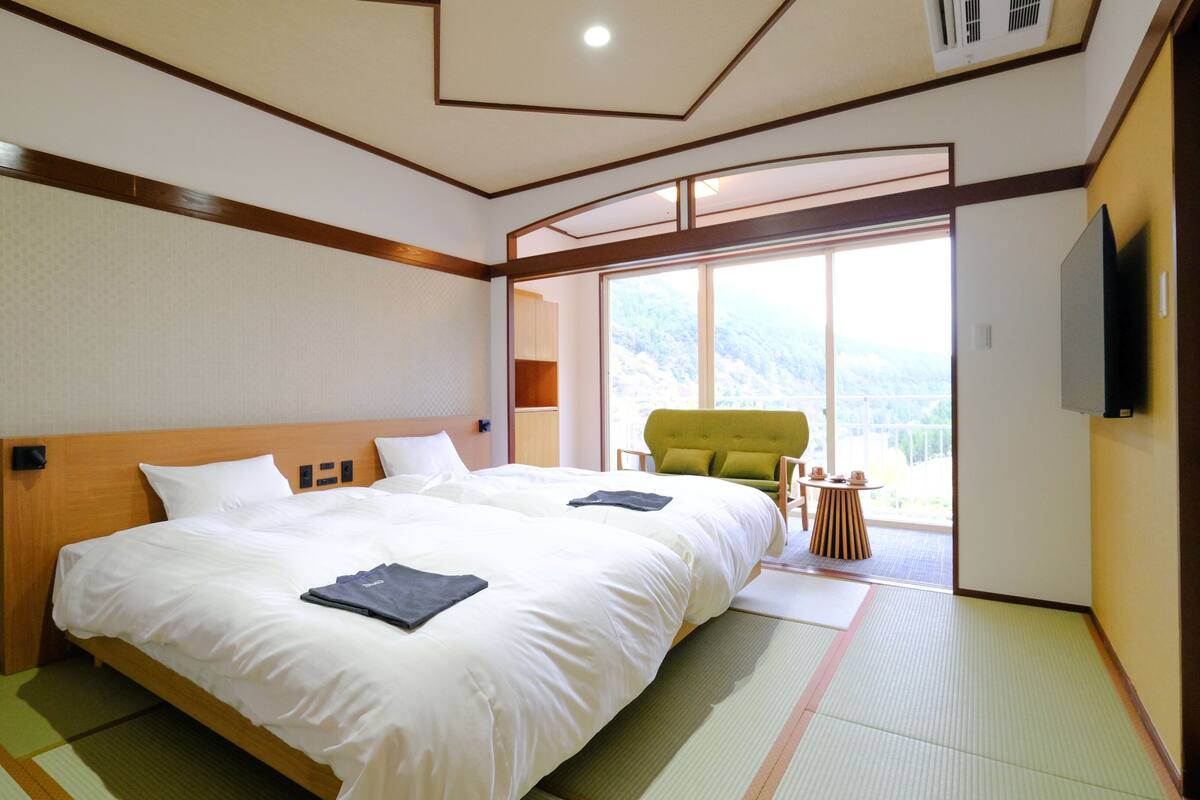 Une chambre d’hôtel avec un grand lit, un fauteuil vert et une vue sur un paysage montagneux, visible à travers une grande fenêtre.