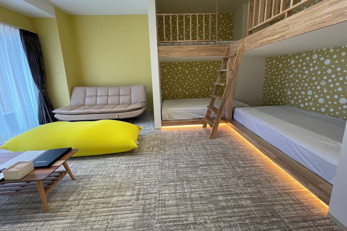 Une pièce avec des lits superposés, un canapé, un coussin jaune et une petite table.