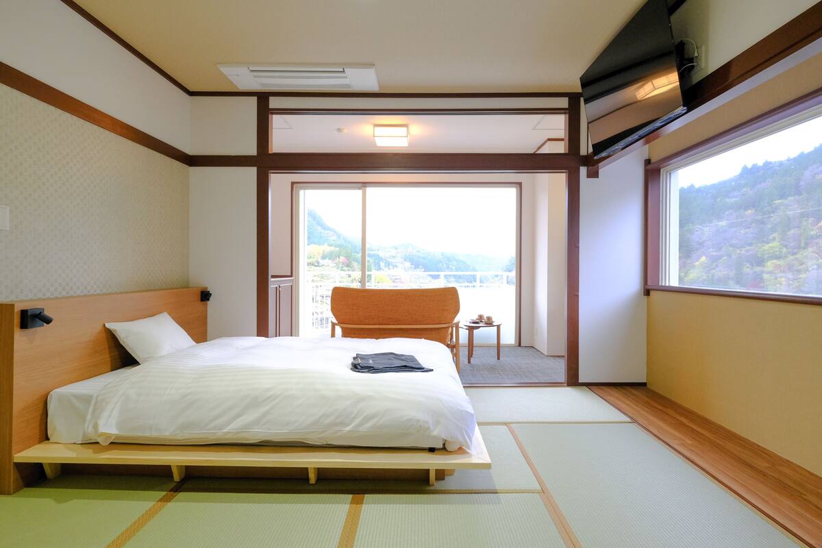 Une chambre d’hôtel avec un lit, une chaise, une petite table et une vue sur un paysage montagneux.